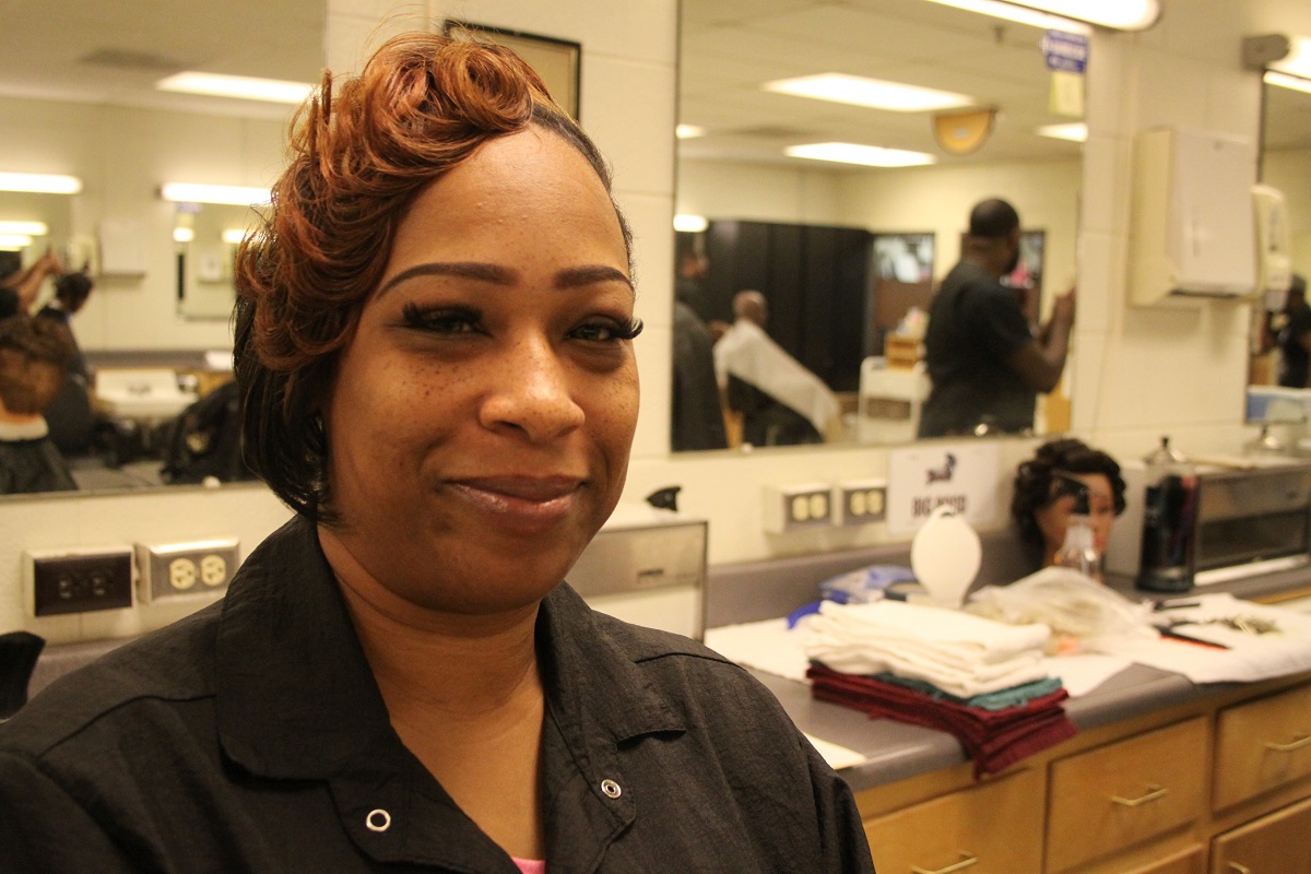 Female in barbering jacket stand behind the chair in the lab.