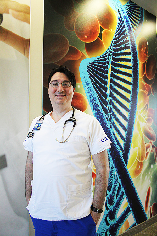 Male Nursing student poses in front of health sciences mural. 
