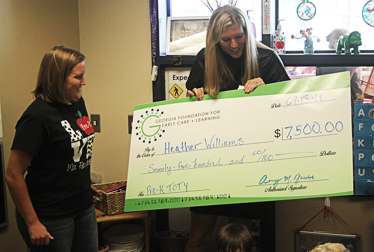 Heather Williams (left) smiles as she is surprised by a representative of Bright from the Start: Georgia Department of Early Care and Learning (DECAL) naming her the 2019-2020 Georgia Pre-K Program Teacher of the Year for a private childcare center.