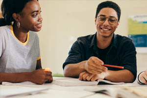 Two students working in notebooks while smiling