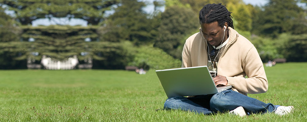 Student sitting in grass with a laptop