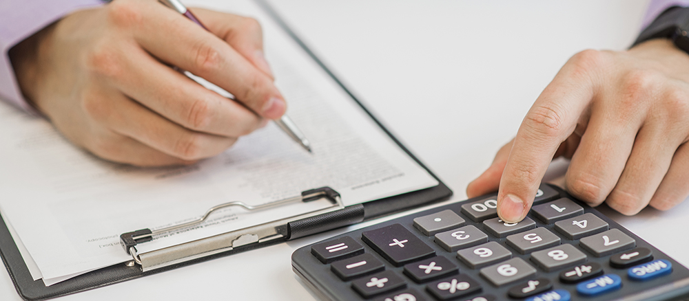 Close-up Of Businessman Calculating Invoices Using Calculator